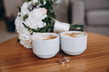 Wedding morning. A wedding bouquet, two cups of coffee and wedding rings lie on the table. aesthetics and details of the wedding