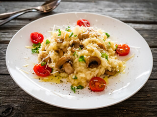 Risotto with white mushrooms, roast tomatoes and parmesan on wooden table
