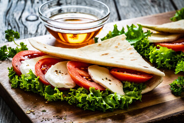 Italian piada wraps - piadina stuffed with fresh lettuce  mozzarella and sliced tomatoes on wooden table