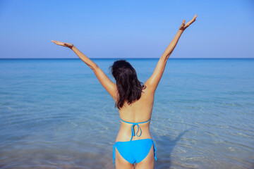 Portrait of beautiful young asian women, wearing blue bikini and stylish white sunglasses standing on the seashore looking at camera smile. Blue sea and sky in the background