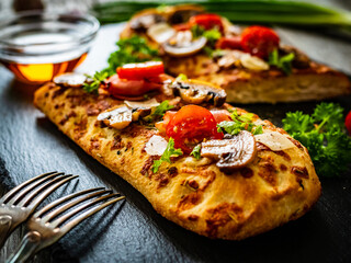 Focaccia - roasted mozzarella sandwiches with white mushrooms, tomatoes and prosciutto ham on black stone plate
