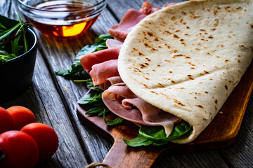 Italian piada wraps - piadina stuffed with fresh vegetable leaves and prosciutto ham on wooden table
