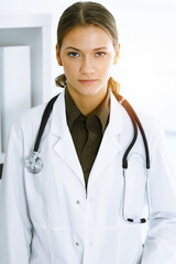 Woman-doctor standing and looking at camera in sunny clinic. Medicine and healthcare