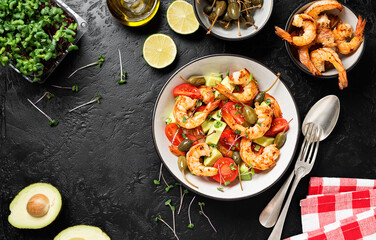 Easy grilled shrimp avocado salad with cherry tomatoes, capers and microgreens. Black background. Top view. Space for text.