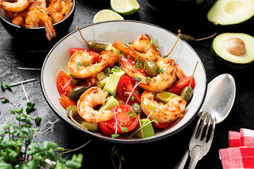 Easy grilled shrimp avocado salad with cherry tomatoes, capers and microgreens. Black background. 