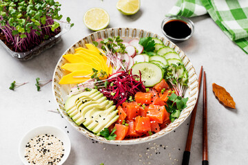 Poke bowl with fresh marinated salmon and variegated vegetables, green onions and microgreens. Gray background