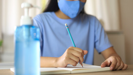 Young Asian woman wearing medical facial handmade mask working alone distancing policy with. Hand sanitizer gel during coronavirus or covid-19 virus outbreak a new normal concept