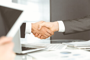 Unknown diverse business people are shaking hands finishing up meeting at the desk in office, close-up. Handshake concept