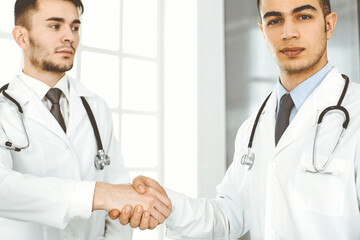 Two doctors are shaking hands as agreement about patient's treatment, close-up. Medical help, medicine concept