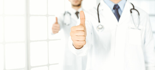 Two male doctors standing as a team with thumbs up in hospital office and ready to help patients. Medical help, best disease treatment and medicine concept