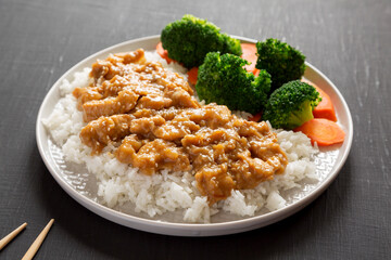 Homemade Orange Chicken with White Rice, Broccoli and Carrot on a plate on a black background, side view.