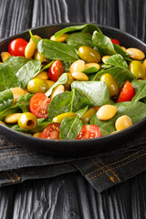 Fresh salad of spinach, lupine beans, tomatoes and olives close-up in a plate on the table. vertical