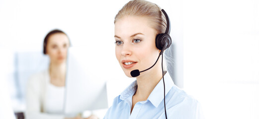 Blond woman call operator is using computer and headset for consulting clients online. Group of...