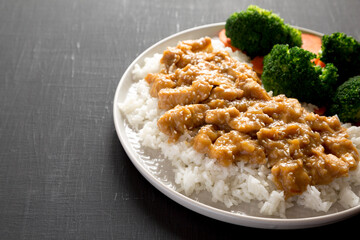 Homemade Orange Chicken with White Rice, Broccoli and Carrot on a plate on a black background, side view. Copy space.