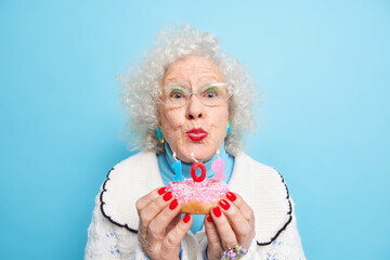 Portrait of good looking senior woman going to blow candles on donut celebrates 102nd birthday...