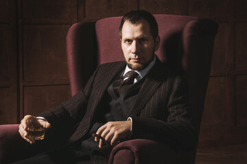 a bearded man sits in luxury leather armchair and relax with cigar and a glass of whiskey