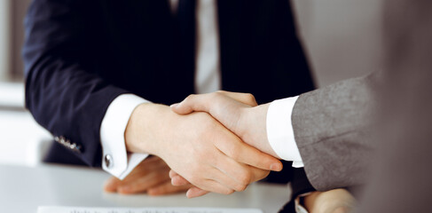 Unknown businessman shaking hands with his colleague or partner above the glass desk in modern office, close-up. Business people group at meeting