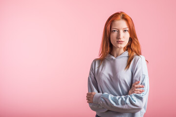 Obraz premium Portrait of a redhead girl who crossed her arms in the studio on a pink background with copyspace