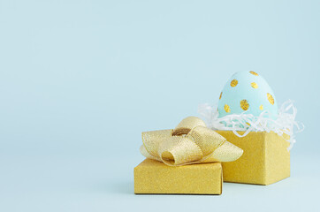Blue easter egg with gold glitter dots in golden gift box on blue background, copy space.