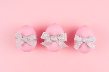 Pink easter eggs with grey bows in row on pastel pink background, top view.