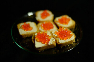 Rusk butter and caviar on a glass plate on a black blur background with space for writing text