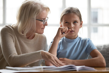 Caring Caucasian old grandmother help teen granddaughter with school homework do assignment at home...