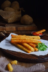 fried potato stick in a wooden board against dark background