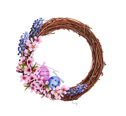 Dry brown rattan wreath with pink and blue spring flowers, Easter eggs and satin ribbon isolated on white