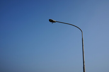 An electric lamp post has a broken light with some materials hanging.  The street light is left...