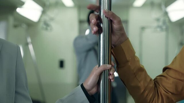 The hand of a man harassing a woman's hand clinging to a rail on a public transportation system at night
