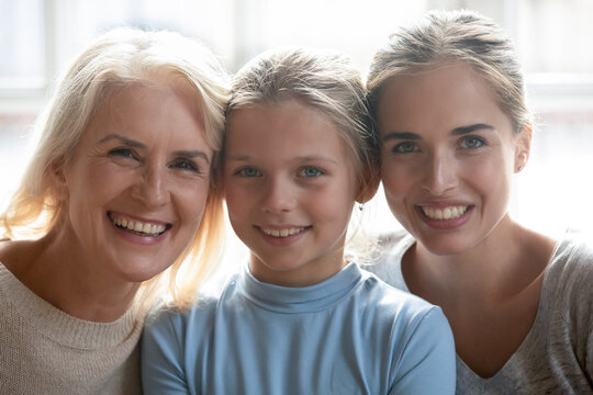 Close up headshot portrait of happy Caucasian three generations of women show family unity pose at home together. Profile picture of smiling little girl child with young mother and senior grandmother.