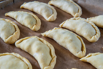 Uncooked empanadas on a baking tray. Traditional Latin American baked beef pastry ready for the oven. Gluten free savory appetizer with meat filling. Handmade typical dish in Spain or Argentina. Side