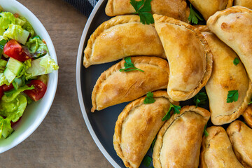 Traditional Latin American baked beef empanadas on a plate with a fresh salad sidedish. Gluten free savory pastries with meat stuffing or filling. Handmade typical dish in Spain or Argentina. Close up