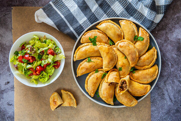 Empanadas. Traditional Latin American baked beef pastry on a plate with fresh salad. Gluten free savory appetizer cut into half with meat filling. Handmade typical dish in Spain or Argentina. top view