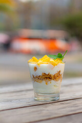 yogurt homemade mango topping layer granola in glass close up on wood table blur background