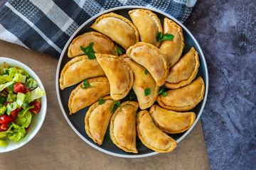 Empanadas - Traditional Latin American baked beef pastry on a plate with a fresh salad sidedish. Gluten free savory pastries with meat stuffing or filling. Handmade typical dish in Spain or Argentina.