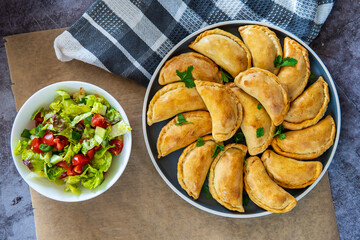 Traditional Latin American baked beef empanadas on a plate with a fresh salad sidedish. Gluten free savory pastries with meat stuffing or filling. Handmade typical dish in Spain or Argentina. Top view