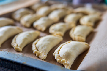 Uncooked empanadas on a baking tray. Traditional Latin American baked beef pastry ready for the oven. Gluten free savory appetizer with meat filling. Handmade typical dish in Spain or Argentina. Side 