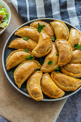 Traditional Latin American baked beef empanadas on a plate with a fresh salad sidedish. Gluten free savory pastries with meat stuffing or filling. Handmade typical dish in Spain or Argentina. Top view