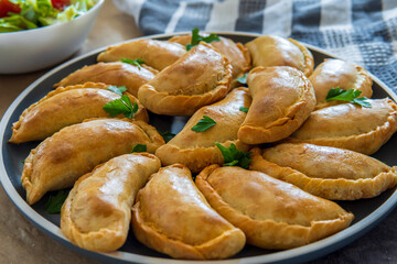 Traditional Latin American baked beef empanadas on a plate with a fresh salad sidedish. Gluten free savory pastries with meat stuffing or filing. Handmade typical dish in Spain or Argentina. Close up