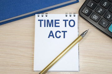the time to act is written on a notebook that lies on a wooden table next to a black calculator and a blue notebook.