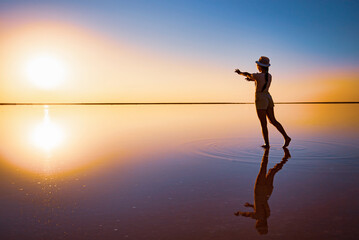 A girl reaches out with her hands to the setting sun on the mirror surface of a salt lake