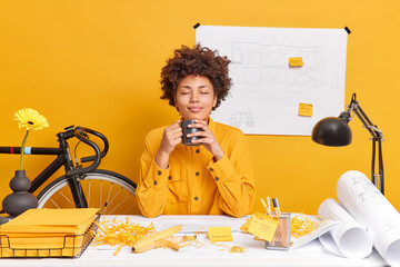 Satisfied relaxed woman architect office worker has coffee break closes eyes from pleasure as...