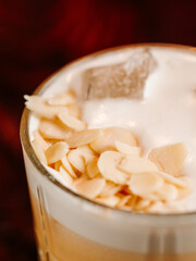 cocktail with white foam, ice cubes and almonds. On a wooden bar