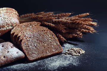 Fresh loaves of bread with wheat and gluten on a black table. Bakery and grocery concept. Fresh, healthy sorts of rye and white loaves food closeup. Fresh homemade bread with cereals.