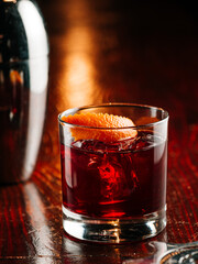 a glass of whiskey with an ice cube and orange peel decor. On a wooden bar