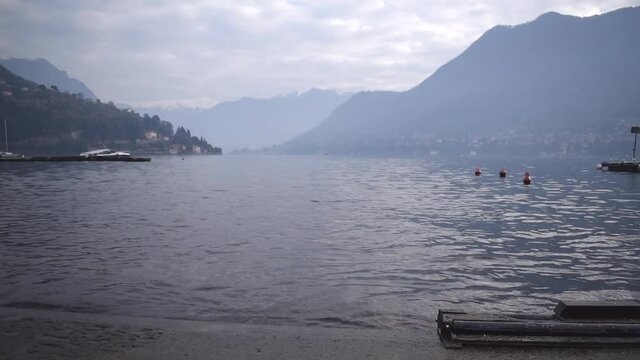 View of Shore Como lake, mountains with snow. wooden pier with boats. Pigeon glides to land.