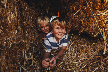 Blonde brothers playing in hay shed smiling at camera. Country kids having fun on rural property. © Caseyjadew