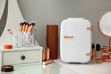 Cosmetics refrigerator and skin care products on white vanity table indoors
