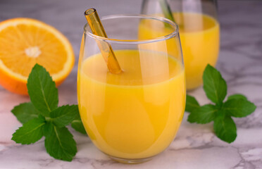Two glasses with fresh orange juice and a sprig of mint on a marble top.